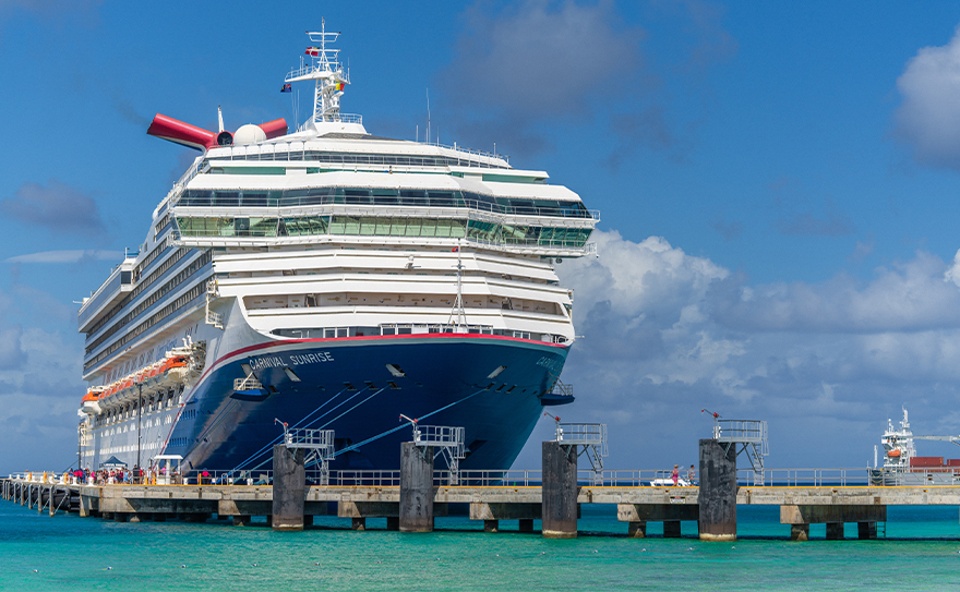 Large Carnival Sunrise cruise ship docked at a pier with a clear blue sky and calm turquoise waters.